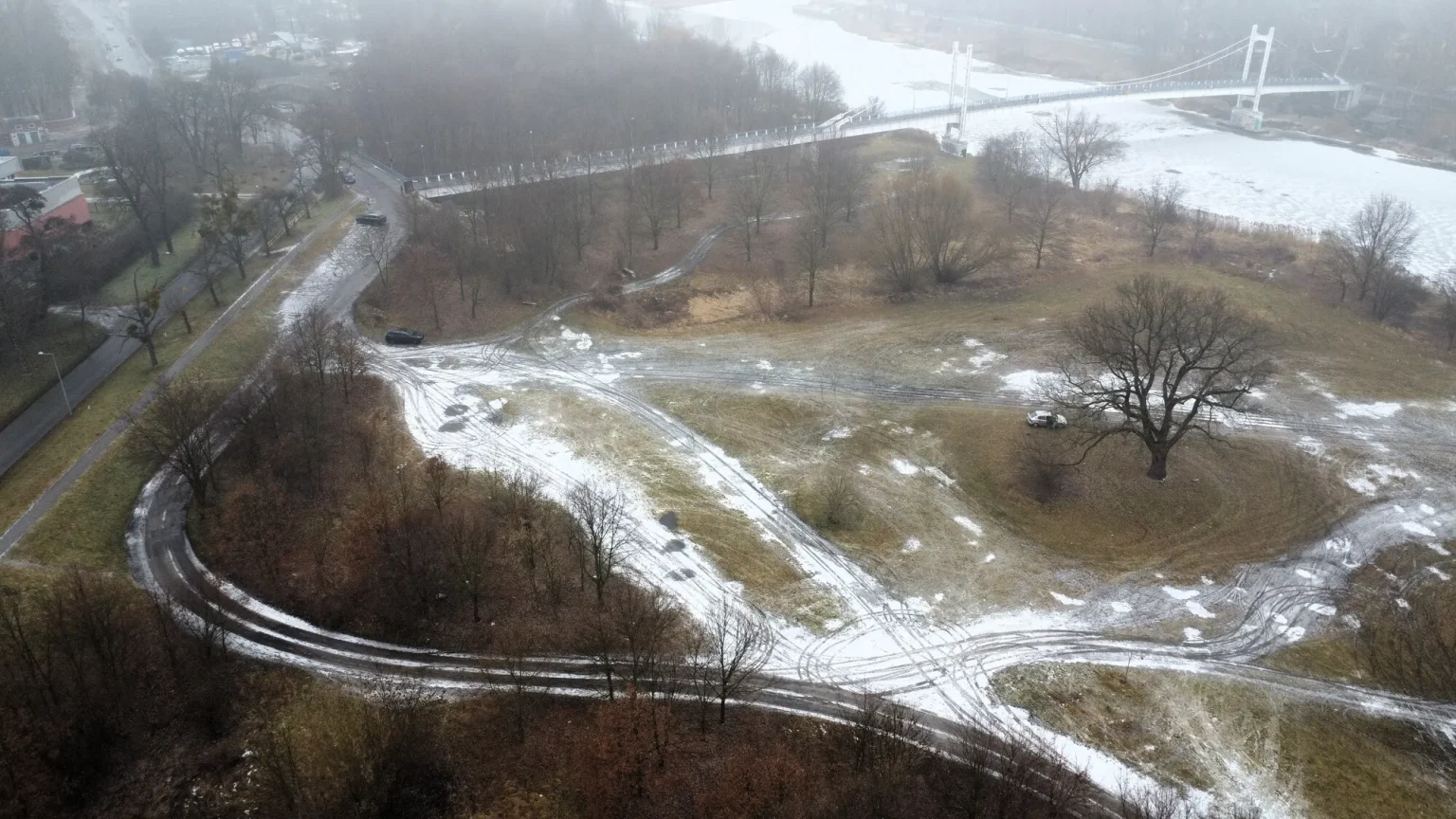 Mglisty widok z lotu ptaka na okolicę ulicy Na Grobli i Międzyrzeckiej we Wrocławiu z kładką nad rzeką i śladami opon na śniegu.