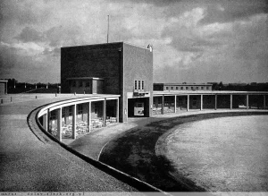 Historyczne czarno-białe zdjęcie przedstawiające modernistyczną architekturę Wieży Maratońskiej oraz dziedzińca honorowego na Stadionie Olimpijskim we Wrocławiu.