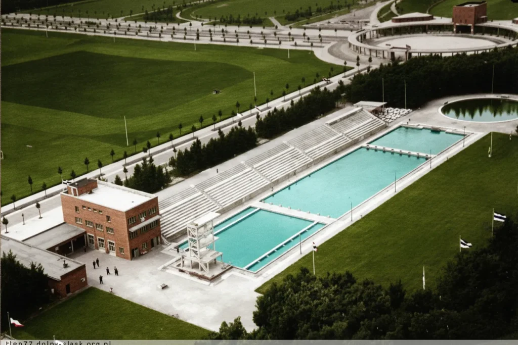 Widok z lotu ptaka na kompleks basenów Stadionu Olimpijskiego we Wrocławiu z 1930 roku, zdjęcie koloryzowane przedstawiające basen pływacki, wieżę do skoków i trybuny.